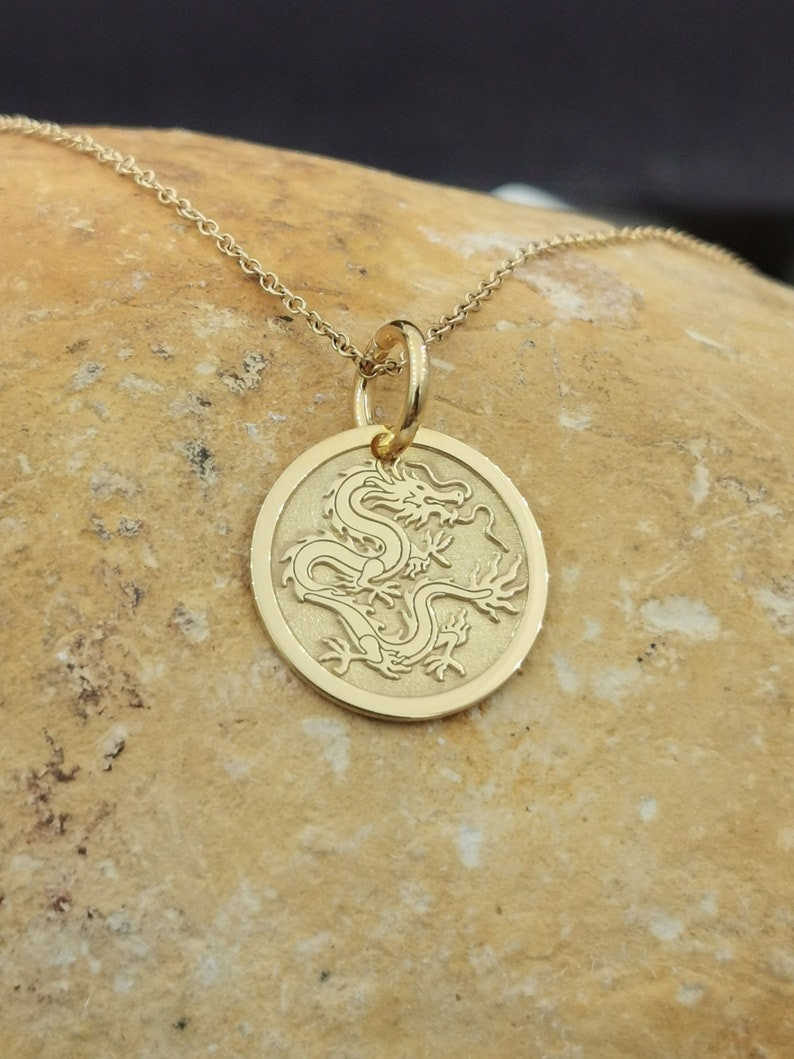 Chinese Dragon engraved, circular,
solid gold pendant 14k,
the size is 0,5 iches / 12,7 millimeter.
Thickness 0,5 milimiters.
The hoop on top is circular and gold as well.
 The finish of the pendant in shinny.