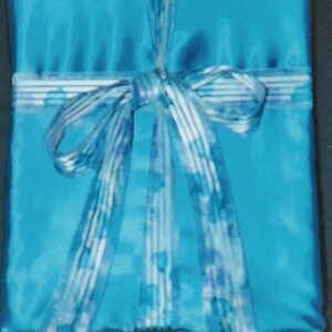 May include: A rectangular gift box wrapped in bright cyan satin fabric. The package is tied with a translucent, light blue ribbon featuring a subtle, repeating pattern of small, darker blue shapes, tied into a decorative bow at the center.