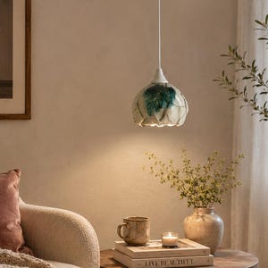 May include: A ceramic pendant light with a scalloped edge and a white and teal glaze finish, suspended from a white cord. The lamp features a glossy, textured surface with organic, petal-like shapes that diffuse light downward in a soft glow.