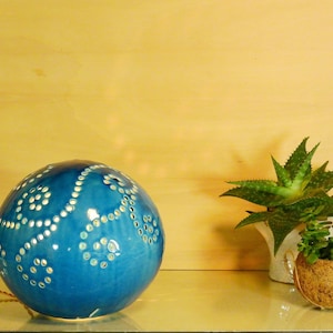 May include: A blue ceramic lamp with a white dot pattern. The lamp is shaped like a sphere and has a cord attached to it. The lamp is sitting on a wooden surface next to a small potted plant.