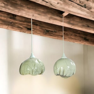 Puede incluir: Dos lámparas colgantes de vidrio verde con acabado craquelado cuelgan de una viga de madera.