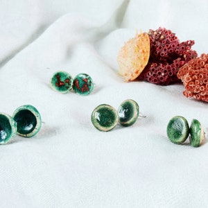 May include: Three pairs of ceramic stud earrings with green and white glaze. The earrings are displayed on a white surface.
