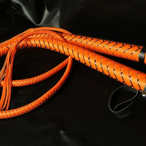 Puede incluir: Un l&aacute;tigo de cuero trenzado con un esquema de color naranja y negro. El l&aacute;tigo tiene un mango trenzado y una borla en el extremo.
