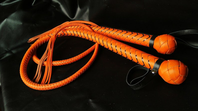 Puede incluir: Un l&aacute;tigo de cuero trenzado con un esquema de color naranja y negro. El l&aacute;tigo tiene un mango trenzado y una borla en el extremo.