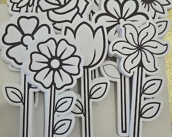 May include: A collection of white foam flower cutouts featuring bold black outlines. Each piece depicts a different floral shape, including daisies, roses, and tulips, all attached to a long, thin stem with two leaves extending from the sides.