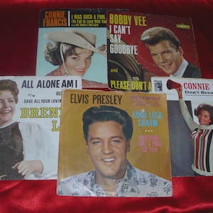 Könnte beinhalten: Eine Sammlung von Vintage-Schallplatten mit Künstlern wie Elvis Presley, Connie Francis und Bobby Vee. Die Albumcover zeigen Porträts und Songtitel, vor rotem Hintergrund.
