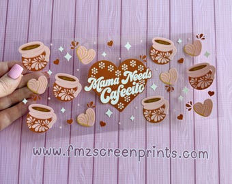 May include: A clear sticker sheet with coffee cups, hearts, and the text "Mama Needs Cafecito." The coffee cups are brown and pink with floral designs. Hearts and star shapes are scattered around the design.