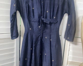 May include: A long, navy blue dress with a zipper closure and a tie at the waist. The dress is covered in small, embroidered white flowers.