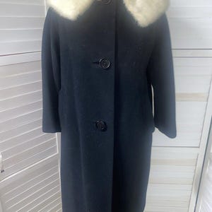 May include: A long black wool coat with a white fur collar. The coat has a button closure and long sleeves.