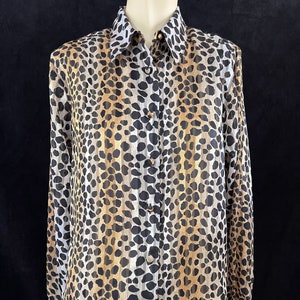 May include: A button-down shirt with a leopard print pattern. The long-sleeved shirt features a collar and a pattern of black and brown spots on a beige background. The shirt is displayed on a mannequin.