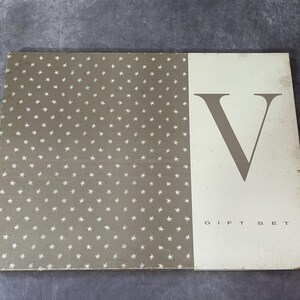 May include: Rectangular gift set box with a two-tone design. The left side features a gray background with white star-shaped patterns. The right side is off-white with a large gray letter "V" and the words "GIFT SET" in a serif font.