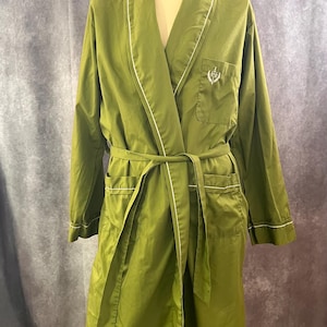 May include: Olive green robe with white trim and a matching belt. The robe has a shawl collar, patch pockets, and a small embroidered emblem on the chest. The robe is displayed on a mannequin.