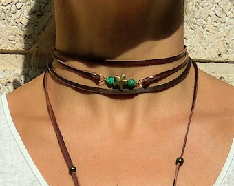 May include: A brown leather lariat necklace with a turquoise and gold charm. The necklace is layered with three strands of leather and has small gold beads.