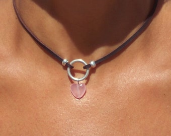 May include: A black leather choker necklace with a silver ring and a pink heart pendant.