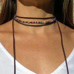 May include: A brown leather choker necklace with multiple strands of colourful beads. The necklace is tied with a long brown leather cord that hangs down the front of the neck.