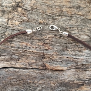 May include: A brown leather cord necklace with silver clasps. The cord is lying on a piece of weathered wood.