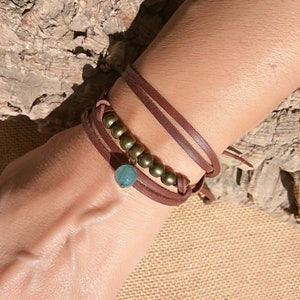 Op de afbeelding: Een bruin leren armband met een turquoise steen en gouden kralen.