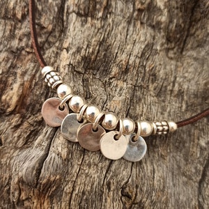May include: A brown leather necklace with silver round charms and beads.