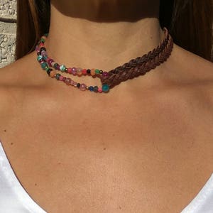 Op de afbeelding: Een bruin leren gevlochten choker ketting met een meerkleurige kralenstreng. De kralen zijn roze, groen, blauw, paars en oranje.