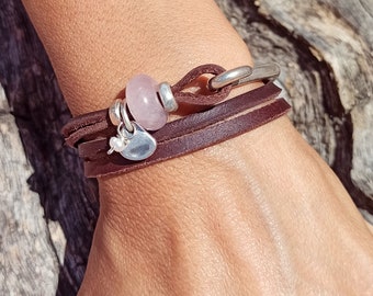 May include: A brown leather wrap bracelet with a silver clasp and a pink gemstone bead. The bracelet has a small silver heart charm.