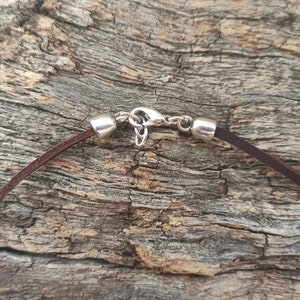 May include: Close-up of a brown leather cord necklace with a silver clasp.
