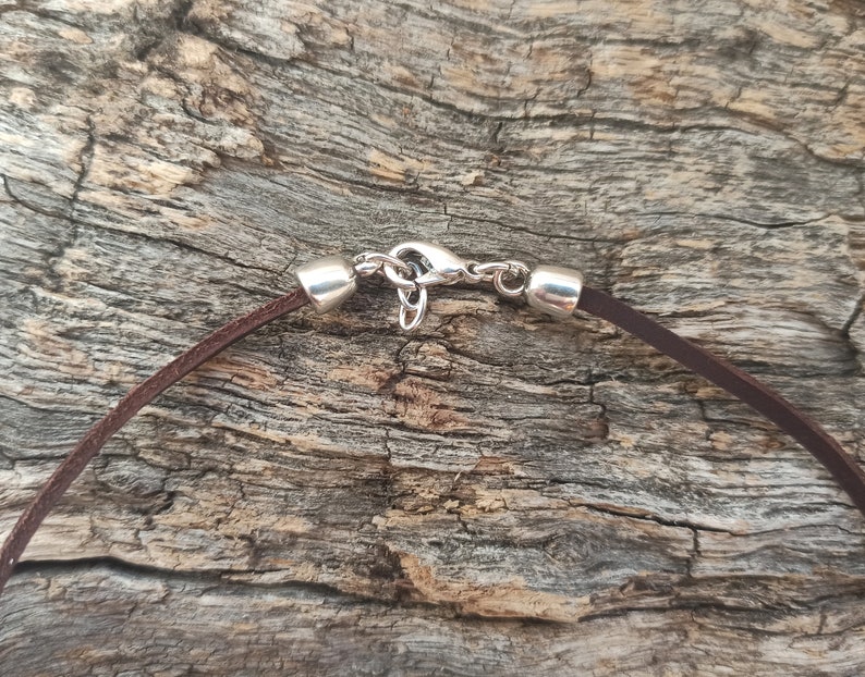 May include: Close-up of a brown leather cord necklace with a silver clasp.