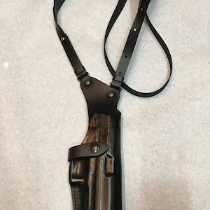 May include: Black leather shoulder holster with adjustable straps and a snap closure. The holster is designed to carry a handgun.