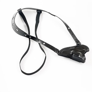 Op de afbeelding: Zwart leren schouderholster voor een pistool. Het holster heeft verstelbare banden en een veilige pasvorm.
