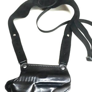 Puede incluir: Una funda de hombro de cuero negro con un compartimento moldeado para arma de fuego, correas de hombro ajustables con textura de ante y herrajes metálicos plateados. El sistema de arnés incluye costuras reforzadas y cierres a presión.