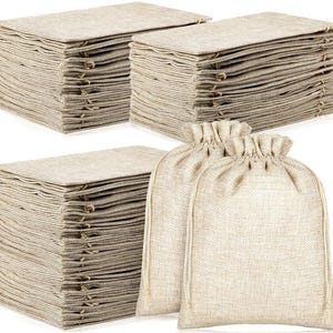 May include: Several stacks of beige burlap fabric squares and two drawstring bags. The fabric squares are neatly arranged in stacks, while the drawstring bags are made of the same beige burlap material. The bags have a gathered top and a drawstring closure.