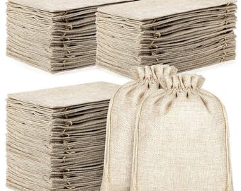 May include: Stacks of beige burlap fabric squares and two drawstring bags. The fabric squares are neatly arranged in stacks, while the drawstring bags are made of the same beige burlap material. The bags have a gathered top and a drawstring closure.