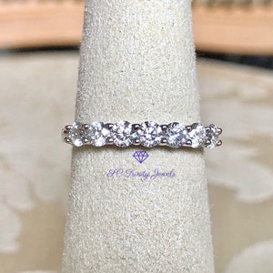May include: A silver band with a row of round, clear gemstones. The band is on a white display stand.