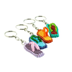 May include: Four beaded flip-flop keychains in different colors: purple, blue, green, and orange. Each keychain has a silver metal ring.