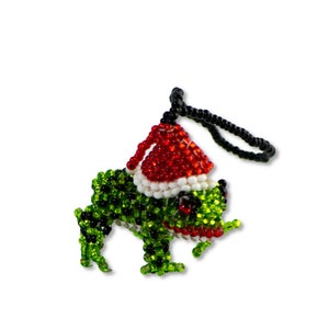 May include: A green beaded frog wearing a red and white beaded Santa hat with a black beaded string for hanging.