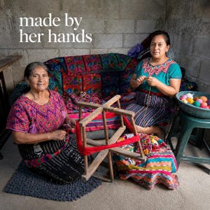 Peut inclure: Deux femmes sont assises, l'une tenant un d&eacute;vidoir en bois avec de la laine rouge, l'autre tricotant. La sc&egrave;ne se d&eacute;roule dans une pi&egrave;ce avec un canap&eacute; &agrave; motifs floraux et le texte "made by her hands". Des boules de fil color&eacute;es sont dans un bol.
