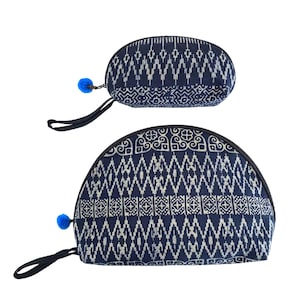 May include: Two half-moon shaped blue and white patterned fabric cosmetic bags with blue pom-poms on the zipper pulls.
