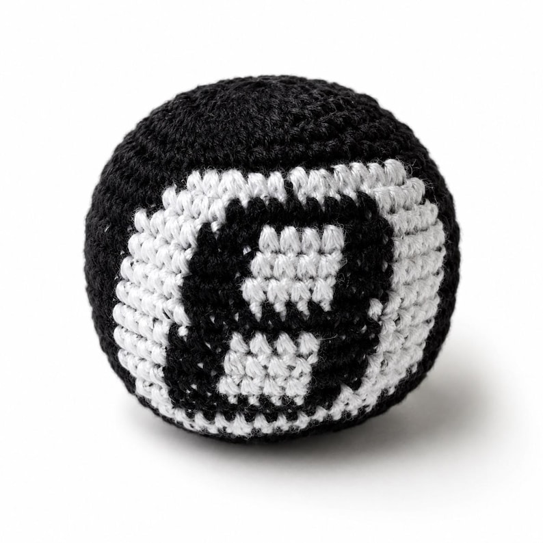 Peut inclure: Une balle crochet&eacute;e noire et blanche, ressemblant &agrave; une boule de billard num&eacute;ro huit. La balle est ronde avec un fond noir et un motif de huit blanc. La texture crochet&eacute;e est visible, sur fond blanc.