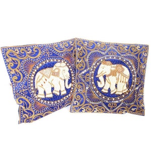 May include: Two blue velvet throw pillows with embroidered white elephants and gold accents. The elephants are surrounded by intricate floral patterns.
