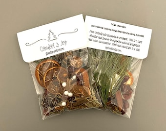 May include: Two clear plastic bags of stovetop potpourri. One bag contains dried orange slices, cranberries, and spices. The other bag has pine sprigs, cinnamon sticks, and dried fruit. Each bag has a white label with the text "Comfort & Joy" and instructions.