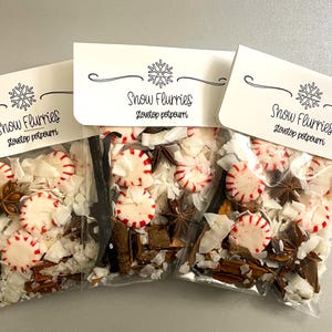 May include: Three clear plastic pouches containing stovetop potpourri with red and white peppermint candies, star anise, cinnamon sticks, and white shavings. Each pouch has a white header card printed with a snowflake and the text Snow Flurries.