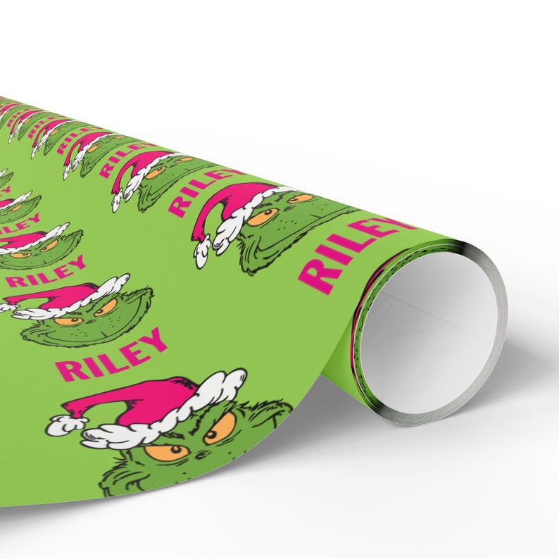 May include: A roll of green wrapping paper featuring a repeating pattern of a cartoon character's face wearing a Santa hat. The name "RILEY" is printed in pink. The paper is rolled up, showing the inside.