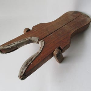 Puede incluir: Un sacabotas de madera vintage con acabado marrón oscuro. El sacabotas tiene una pieza de metal curvada en cada extremo y un asa en el lateral. El sacabotas está diseñado para ayudar a quitar las botas.