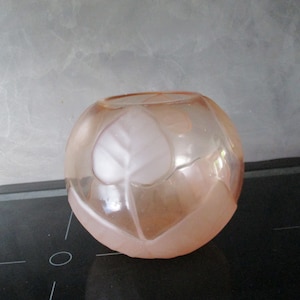 May include: A round, frosted glass vase with a pink hue and a design of leaves etched into the surface.