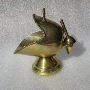 Puede incluir: Un azucarero de latón vintage con un diseño en forma de cuchara. El azucarero presenta un asa y un patrón decorativo en la tapa. Se asienta sobre una base redonda de pedestal. El latón tiene un acabado dorado pulido.