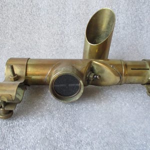 May include: A brass telescope with a round viewing lens and a side-mounted brass tube. The telescope is attached to a metal bracket with a screw.