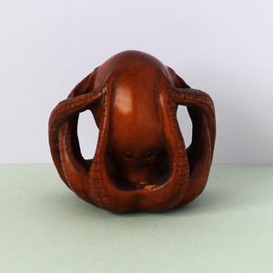 May include: A carved wooden octopus sculpture. The octopus is a rich brown color with detailed carving of the tentacles and body. The sculpture is a unique decorative item.