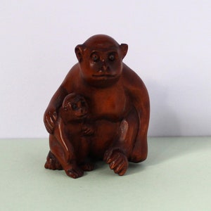 May include: A wooden carving of a monkey holding a smaller monkey. The monkeys are brown and have detailed features.