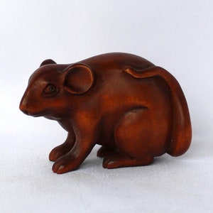 May include: A small, intricately carved wooden sculpture of a brown mouse. The mouse is sitting with its tail curled around its body.
