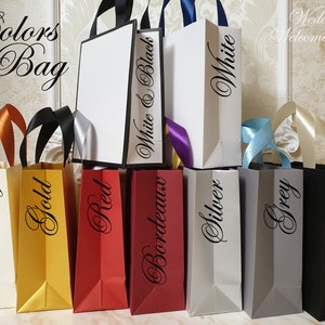 May include: A collection of colorful gift bags with various ribbon handles. The bags are in shades of ivory, gold, red, bordeaux, silver, grey, and black. Each bag has a color name printed on it. The text "Colors of Bag" and "Wedding Welcome Bag" are also visible.