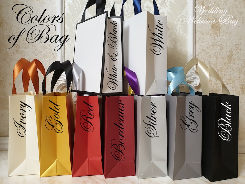 May include: A collection of colorful gift bags with various ribbon handles. The bags are in shades of ivory, gold, red, bordeaux, silver, grey, and black. Each bag has a color name printed on it. The text "Colors of Bag" and "Wedding Welcome Bag" are also visible.
